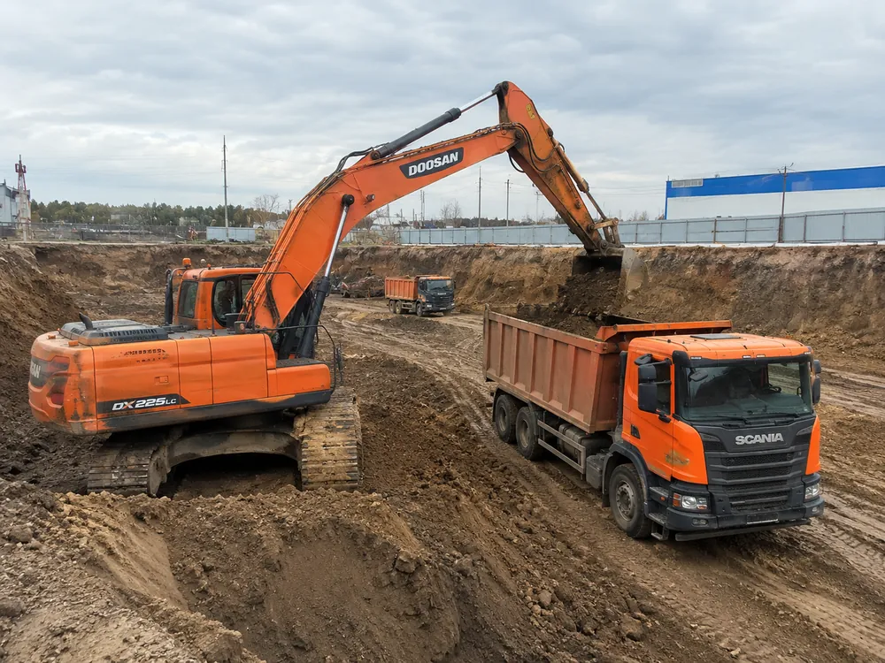 Экскаватор Doosan DX225 грузит грунт в самосвал на котловане